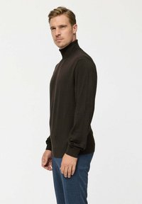 Sötétbarna garbó pulóver hosszú ujjal, puha anyagból készült, testhez álló szabású, bordázott mandzsettával, kék nadrággal párosítva.