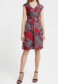 Tomatenrotes und schwarzes, gemustertes Kleid mit kurzen Ärmeln, einem Knoten-Detail an der Taille und einem schwingenden Rock. Es verfügt über geometrische und florale Designs.