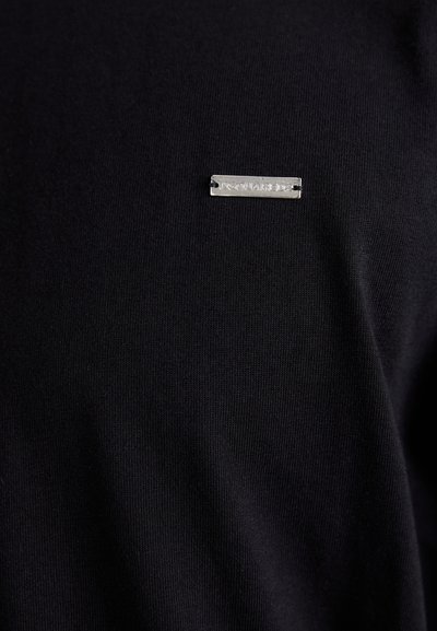 Maglietta nera in tessuto morbido. Presenta un'etichetta logo rettangolare argento sul lato sinistro, ben visibile.