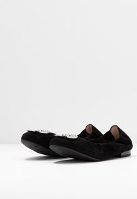 Sorte ruskindssko med rund tå og lille hæl. Har et sølvfarvet hardware-accent foran med en glat overflade og minimalistisch design.