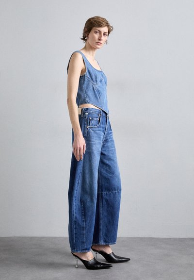 Denim kratki top i široke traperice visokog struka u srednje plavoj boji. Top ima koso šivanje, dok traperice imaju prednje džepove i neuredan rub.