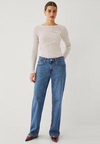 Haut à rayures à manches longues en blanc et marron, associé à un jean large bleu. La tenue présente une silhouette ajustée avec une texture en denim classique.