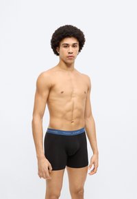 Μαύρα boxer briefs με μπλε μέση που φέρει τη σήμανση "TOMMY HILFIGER". Λείο ύφασμα, σχεδίαση μεσαίου ύψους και εφαρμοστή γραμμή.