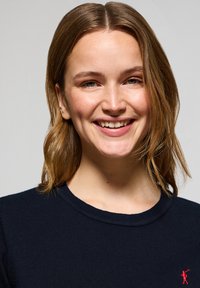 Granatowy sweter dzianinowy z okrągłym dekoltem, z małym czerwonym logo na lewej piersi oraz ribbowanym wzorem.