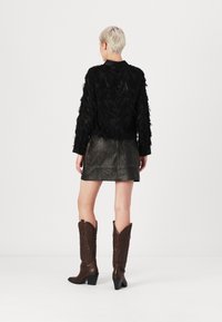 Giacca nera con texture e dettagli simili a piume, abbinata a una mini gonna di pelle scura e stivali cowboy marroni a fantasia.