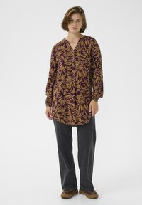 Chemise à manches longues de couleur violet foncé ornée d'un motif de feuilles dorées, avec un col henley et un ourlet arrondi, associée à un pantalon large gris foncé.