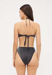 Juodas halterio stiliaus bikinis su blizgia medžiaga. Kaklo ir nugaros raišteliai, aukštai pažeminti apatiniai, glotni tekstūra, minimalistinis dizainas.