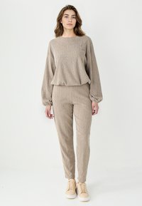 Ensemble de jogger beige en velours côtelé fait de tissu texturé, comprenant un haut ample et un pantalon fuselé, accompagné de baskets crème. Design léger et décontracté.