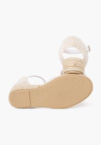 Sandal en espadrille beige tissé avec des sangles blanches, une semelle intermédiaire en jute épaisse et une semelle en caoutchouc texturée. Comprend une sangle réglable à la cheville.