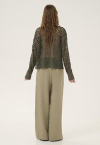 Olivengrøn blonde cardigan med bølget kant og lange ærmer, parret med løse beige vidde-bukser. Tekstureret stof og lagdelt design.