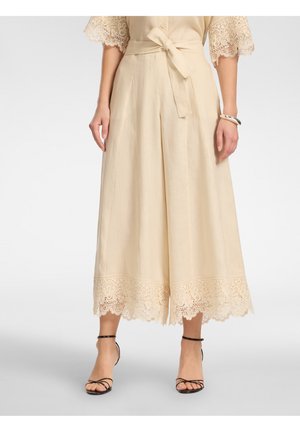 Beige wide-leg cropped pants with lace trim at hem, tied waist belt, worn with black strappy high-heeled sandals.