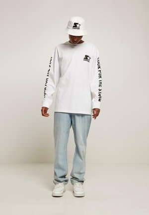 White long-sleeve shirt with black "STARTER" branding, paired with light blue jeans and a matching white bucket hat.