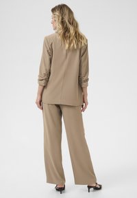 Beige dvoudílný outfit skládající se z volného topu s ohrnutými rukávy a širokými kalhotami. Hladká tkanina s minimálními detaily.