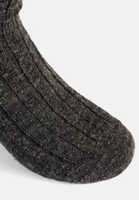 Calcetín de color gris oscuro, tejido, con textura acanalada, punta redondeada y superficie ligeramente pelusa. Presenta un diseño simple sin logotipos visibles.