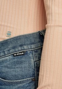 Jasnoróżowa, prążkowana bluzka z długim rękawem w połączeniu z niebieskimi dżinsami. Widoczne logo marki: "G-STAR" na dżinsach oraz "G RAW" na bluzce.