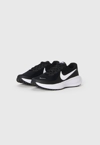 Et par svarte Nike-løpesko med hvit swoosh-logo og tykke hvite såler på en enkel lys grå bakgrunn.