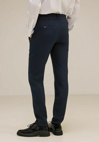 Navy trousers with a slim fit, elastic waistband, and two back pockets, paired with black shoes. Fabric has a smooth texture.
