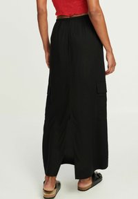 Černá maxi sukně s volným střihem, s dvěma bočními kapsami a rozparkem vzadu. Vyrobena z lehké látky s hladkým povrchem.