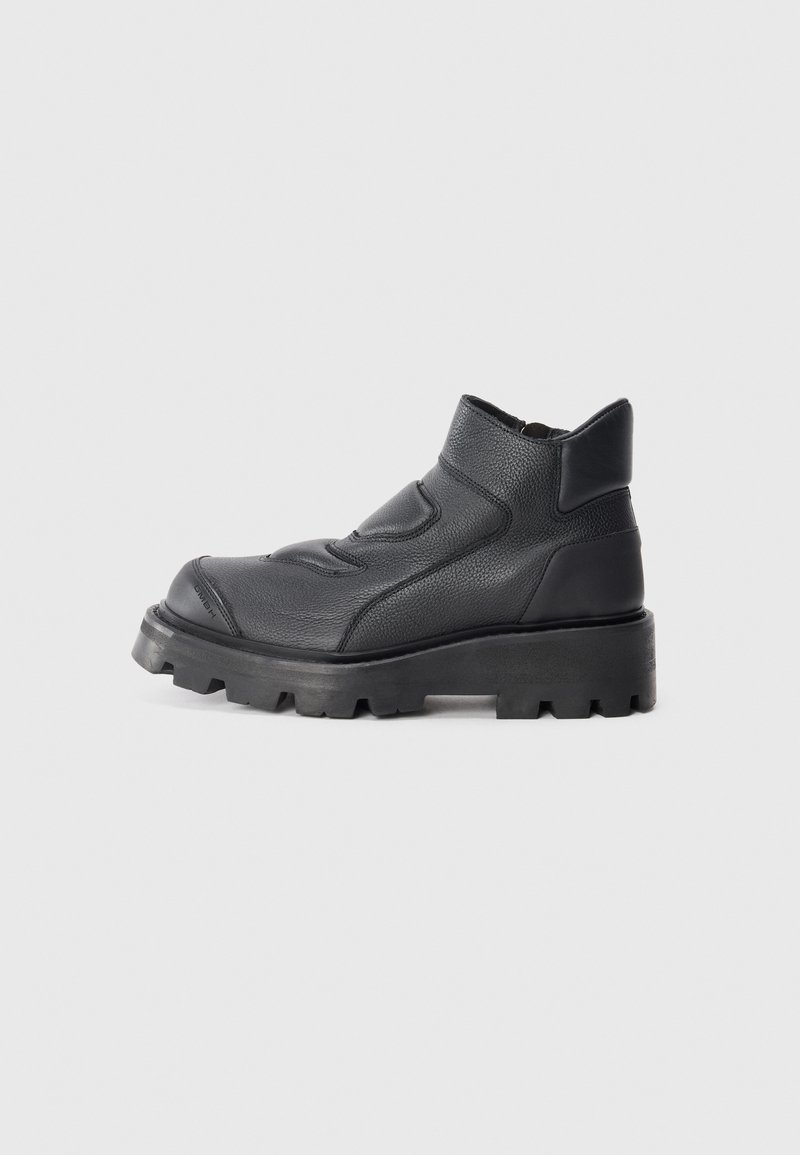 Bota negra de cuero hasta el tobillo con un acabado texturizado, punta redonda, suela de goma gruesa y costuras de acento mínimas. Tacón elevado para mayor altura.