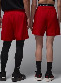 Røde sportsshorts med en glat tekstur, elastisk talje og sidelommer, parret med sorte leggings og sko.