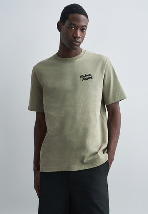 Oliven grøn bomulds t-shirt med korte ærmer, rund halsudskæring og sort broderet "Maison Kitsuné" logo på brystet.