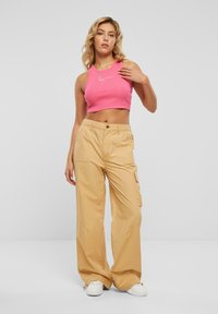 Rosa stripete crop top med hvit logo, sammen med beige cargo bukser med sidelommer. Modell i hvite joggesko. Enkel bakgrunn.