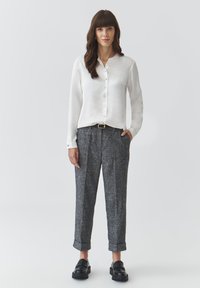 White, button-up blouse with a soft sheen, paired with gray, textured tapered trousers, featuring rolled cuffs and black loafers.