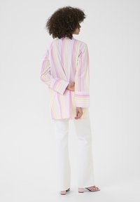 Multicolored striped long shirt in pink, yellow, and white, featuring long sleeves and a relaxed fit, paired with white flared pants.