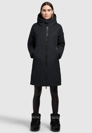 Black insulated coat with a large hood, front zipper, and side pockets. Worn over black leggings and knee-high black boots.