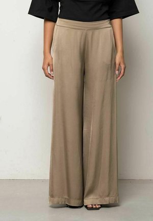 Persona che indossa pantaloni beige a vita alta e gamba larga con tasche laterali, abbinati a top nero e sandali neri con punta quadrata.