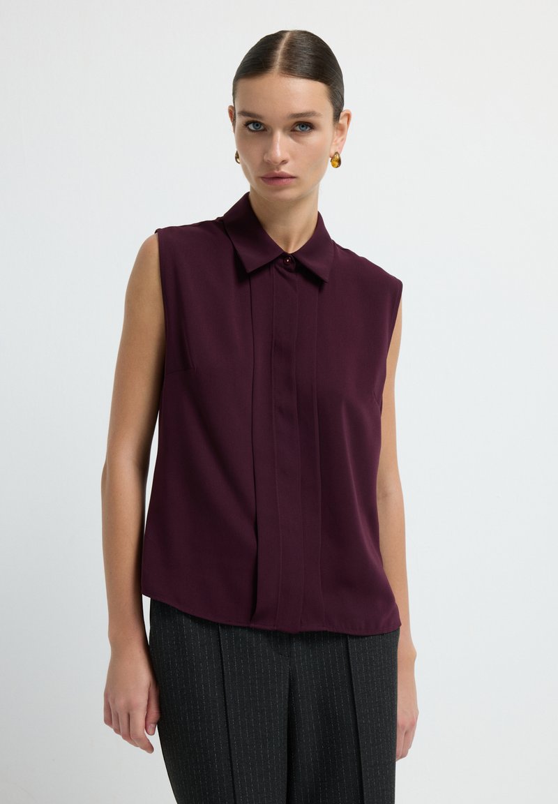 Blusa senza maniche bordeaux con colletto, patta frontale con bottoni e dettagli di pieghe sottili. Tessuto morbido con vestibilità su misura.