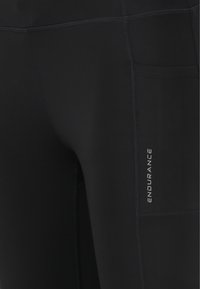 Musta urheilullinen legginsit, jotka on valmistettu joustavasta materiaalista. Niissä on kaiverrettu logo, litteät saumat ja sivutasku säilytystä varten.