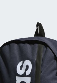 Mochila azul marino con una tela texturizada, con un asa superior, una correa de acento negra y un gran logo blanco en la parte frontal.
