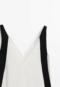 Ærmeløs top med V-udskæring, prydet med sorte, hvide og beige paneler. Lavet af letvægtsstof, der viser en glat tekstur.