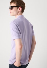 Lys lilla polo skjorte laget av bomull, med korte ermer og klassisk krage. Båret med mørke jeans og svarte solbriller.
