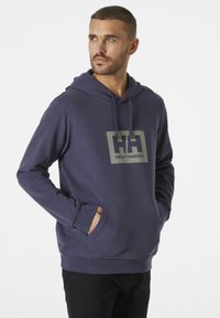 Sudadera azul marino hecha de tejido suave, con un gran logo gris de Helly Hansen en el pecho y un bolsillo canguro en la parte frontal.