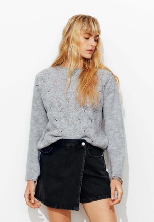 Pull en tricot gris clair avec un motif texturé, associé à une mini-jupe en denim noir avec bouton et poches avant.