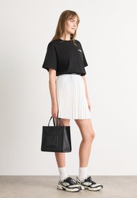 Svart T-skjorte med kort erme, hvit plisséskjørt, svart håndveske med håndtak, hvite sokker og multik colorerte joggesko.
