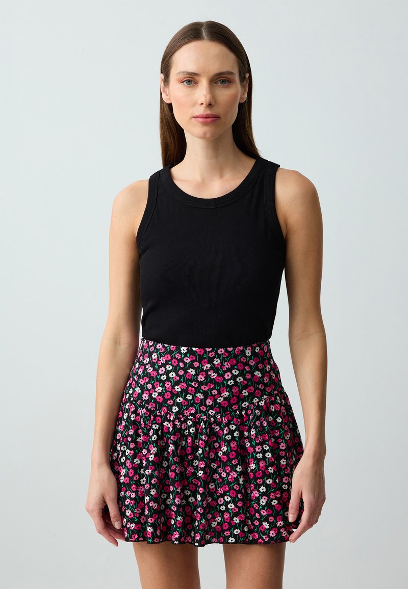 Schwarzes, geripptes Tanktop kombiniert mit einem ausgestellten Minirock, der ein florales Muster in Pink, Weiß und Grün auf schwarzem Hintergrund hat.