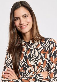 Long-sleeve button-up shirt with a black base featuring abstract orange and cream leaf patterns. Paired with a silver shell pendant necklace.