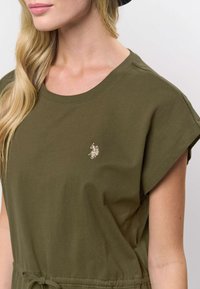 Bavlnené tričko olivovo zelenej farby s krátkymi rukávmi, so zaobleným výstrihom a malým vyšívaným logom na hrudi. Hladká textúra, ležérny strih.