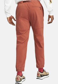 Příjemně hnědé, lehké kalhoty s elastickými manžetami, bočními kapsami a zipovou zadní kapsou, s hladkým povrchem a zúženým střihem.