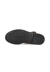 Zwarte rubberen zool met een gestructureerd loopvlakpatroon met driehoekige noppen, bevestigd aan een bruine stoffen bovenkant met een banddetail.