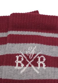 Röda och grå randiga strumpor av stickad tyg, med en vit broderad logotyp med korsade symboler, mjuk textur och ribbad topp.