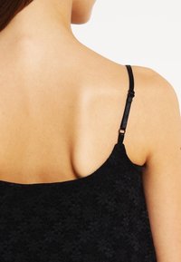 Sort blonde top med tynde justerbare stropper, prydet med blomstertekstur og en dyb udskæring i ryggen. Enkel design og glat stof.