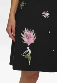 Vestido de tela negra con diseños bordados coloridos: una flor rosa, una figura bailando, estrellas doradas y estrellas azules como acentos.