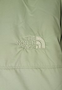 Svetlozelená bunda vyrobená z textúrovaného materiálu so vyšitým logom "The North Face" v krémovej farbe. Hladký povrch s viditeľnými švami.