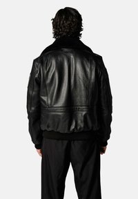 Veste en cuir noir avec un col en fourrure noire douce. Comprend une taille et des poignets côtelés, ainsi qu'une finition lisse et brillante. Convient pour un usage décontracté.