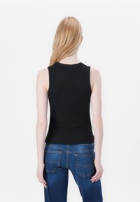 Černý bezrukávový ribbed top s kulatým výstřihem, spárovaný s modrými džíny z denimu, které mají dvě zadní kapsy a mírný efekt zakysaného praní.