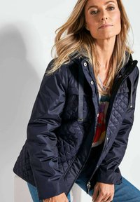 Marineblauwe gewatteerde jas met een capuchon, voorzien van zilveren hardware, schouderbanden en een gladde, glanzende stofstructuur.